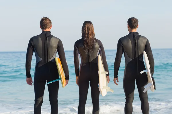 Amigos em fatos de mergulho com prancha de surf na praia — Fotografia de Stock