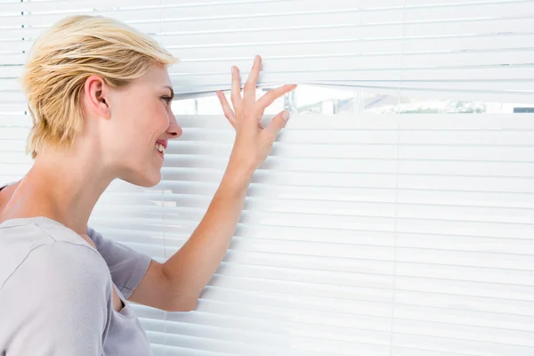 Curious woman looking through venetian blind — Stock Photo, Image