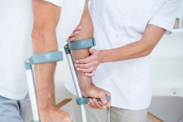 Doctor helping her patient walking with crutch — Stock Photo, Image