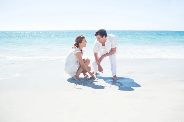 Casal feliz desenhando forma de coração na areia — Fotografia de Stock