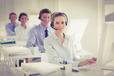Business team working on computers and wearing headsets clipart