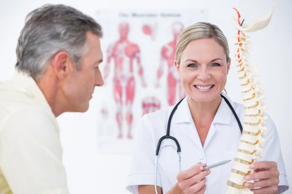 Lachende arts tonen haar patiënt een wervelkolom model — Stockfoto
