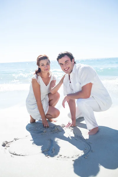 Happy couple drawing heart shape in the sand — Stock Photo, Image