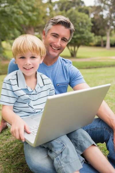 Lycklig far med sin son med laptop i parken — Stockfoto