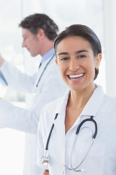 Vrouwelijke arts glimlachend in de camera terwijl haar collega — Stockfoto