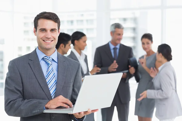 Businessman using laptop with colleagues behind Stock Picture