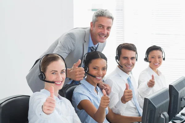 Colleagues with headsets using computers while gesturing thumbs — Stock Photo, Image