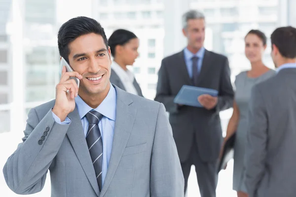 Empresario usando teléfono móvil con colegas detrás —  Fotos de Stock