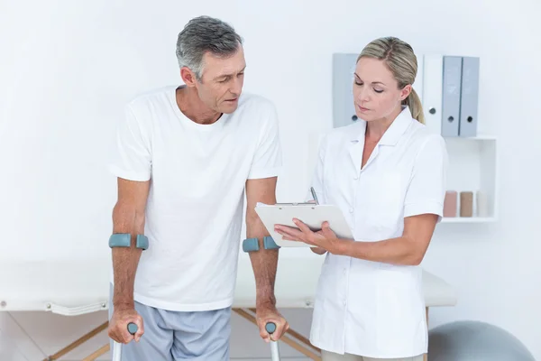 Doctor showing clipboard to her patient with crutch — Stock Photo, Image