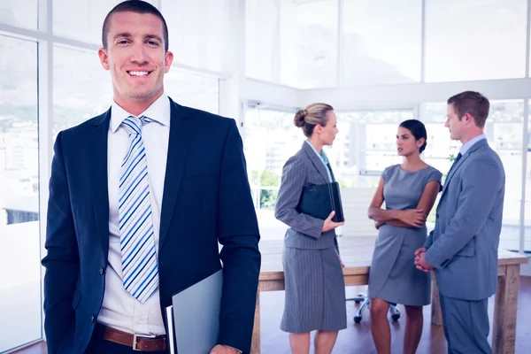 Geschäftsmann lächelt mit Kollegen im Rücken in die Kamera — Stockfoto