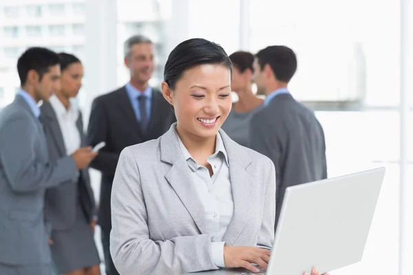 Empresaria usando laptop con colegas detrás — Foto de Stock