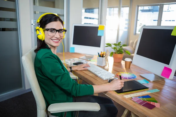 Morena sonriente trabajando en su escritorio y escuchando música —  Fotos de Stock