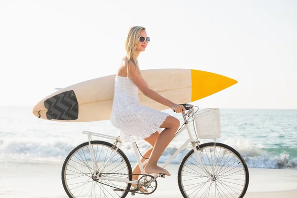 Woman riding bicycle holding surfboard — ストック写真