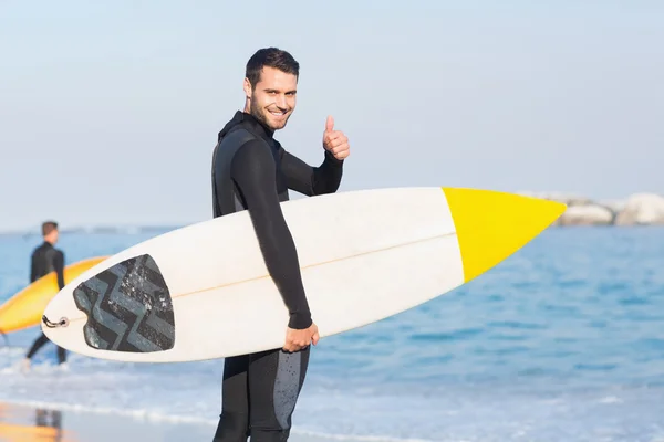 Hombre en traje de neopreno con tabla de surf en la playa —  Fotos de Stock