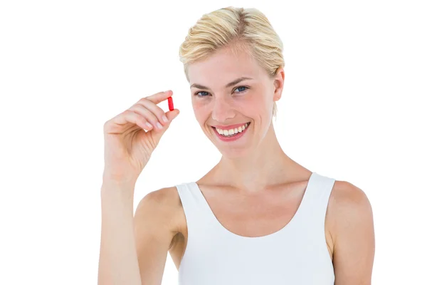 Smiling woman looking at red pill — Stock Fotó