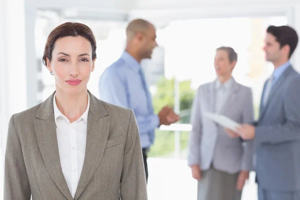 Geschäftsfrau lächelt in die Kamera, während ihre Kollegen diskutieren — Stockfoto