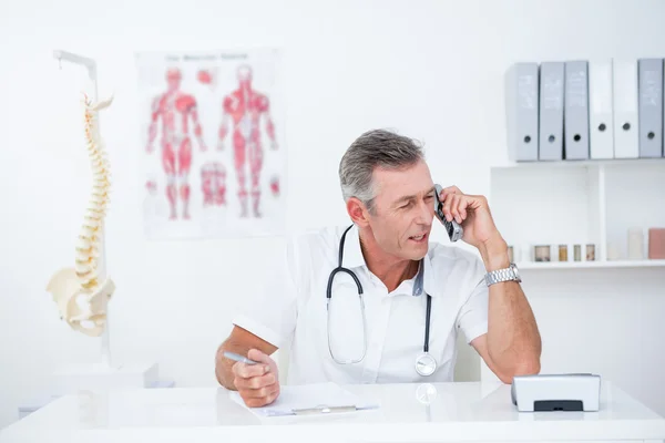 Médico escrevendo na área de transferência e telefonando — Fotografia de Stock