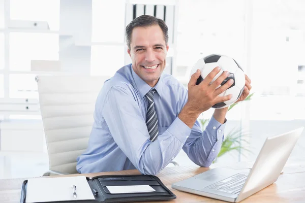 Smiling businessman looking at camera with foot ball — Stock fotografie