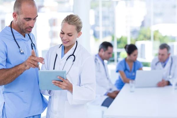 Two doctors looking at clipboard while their colleagues working — Stock Photo, Image