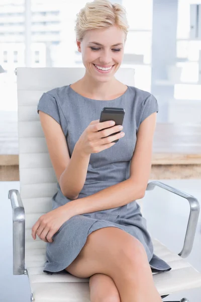 Smiling businesswoman sending a text at her desk — 图库照片