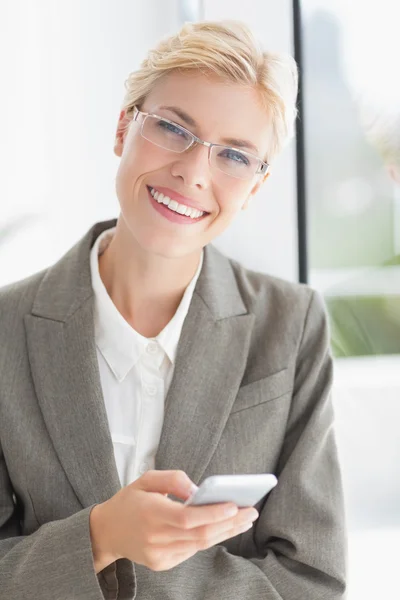 Businesswoman looking at camera and using her smartphone — Stockfoto