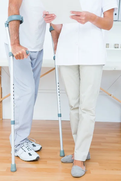 Doctor showing clipboard to her patient with crutch — Stock Photo, Image