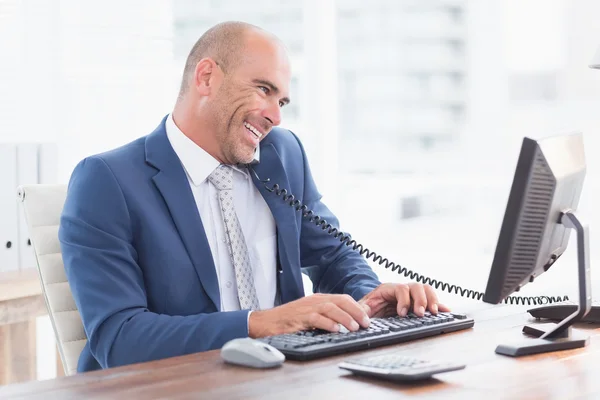 Smiling businessman on the phone and using his computer — Stockfoto