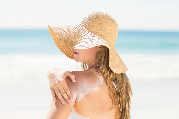 Pretty blonde woman spreading sun tan lotion on her shoulder — Stockfoto