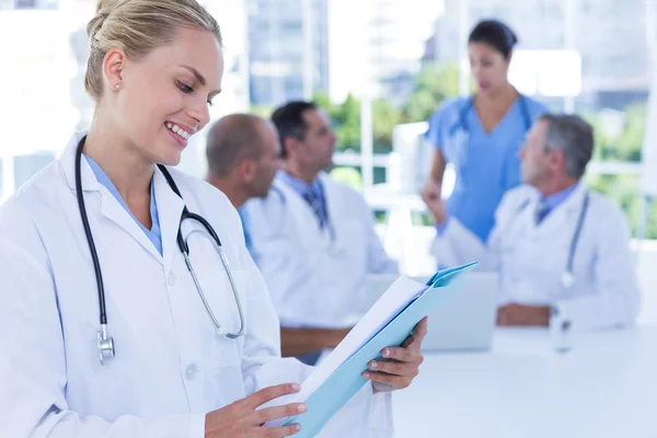 Sonriente doctora mirando el portapapeles mientras sus colegas — Foto de Stock