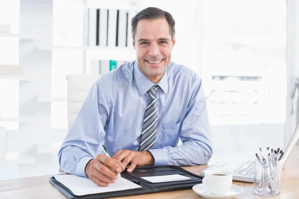 Un hombre de negocios sonriente escribiendo en un papel Imagen de archivo