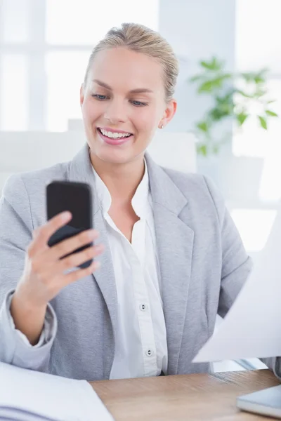 Smiling businesswoman sending a text at her desk — Stockfoto