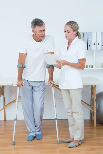 Doctor showing clipboard to her patient with crutch — Stock Photo, Image
