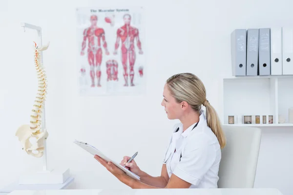 Doctor writing on clipboard at her desk — Stock Photo, Image