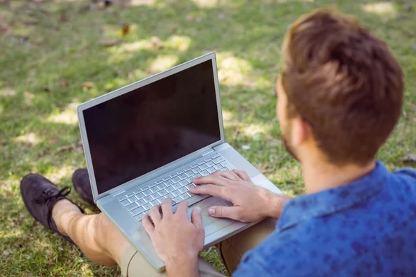 Mladý muž přes notebook v parku — Stock fotografie