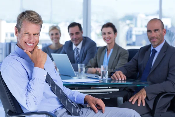 Empresario sonriendo a la cámara con colegas detrás — Foto de Stock