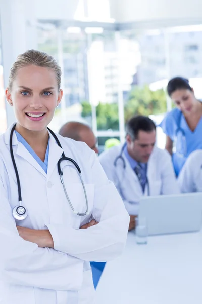 Uśmiechnięta kobieta lekarz patrząc na kamery podczas jej koledzy wor — Zdjęcie stockowe