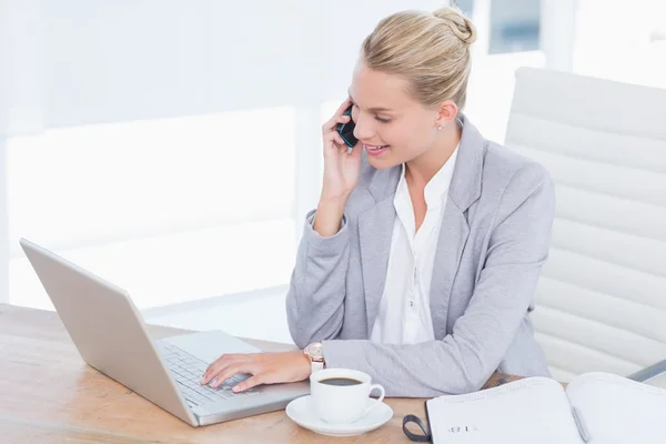 Lächelnder Geschäftsmann, der an ihrem Schreibtisch telefoniert, während sie ihren Computer benutzt — Stockfoto