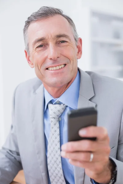 Smiling businessman sending a text at his desk — 图库照片