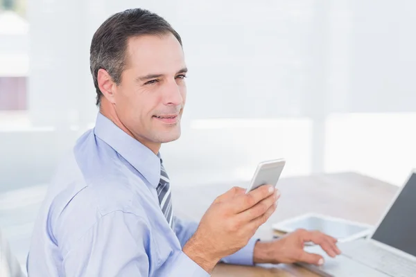 Smiling businessman sending a text at desk — Stock Photo, Image