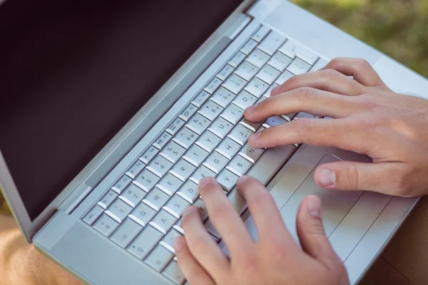 Mladý muž přes notebook v parku — Stock fotografie