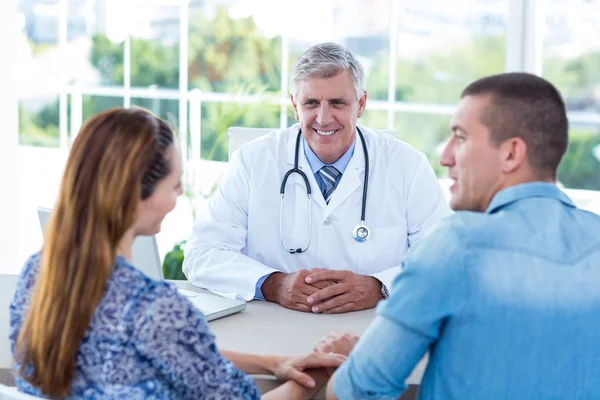 Médico sonriente mirando a pareja feliz —  Fotos de Stock