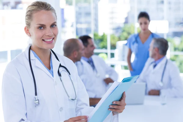 Lächelnde Ärztin blickt in die Kamera, während ihre Kollegen arbeiten — Stockfoto