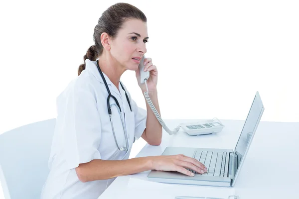 Arzt arbeitet am Laptop und telefoniert — Stockfoto
