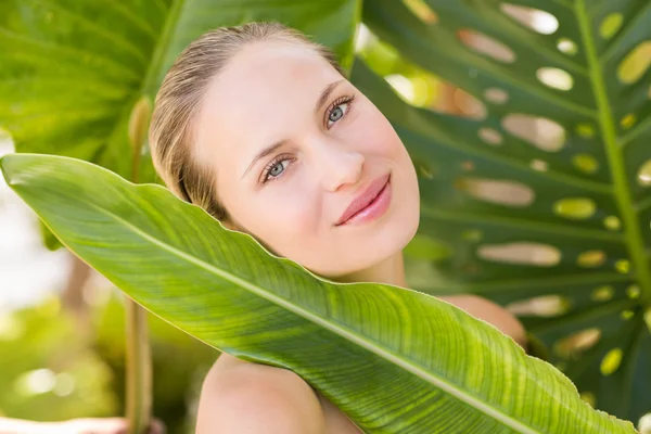 Hermosa rubia sonriendo a cámara detrás de la hoja — Foto de Stock