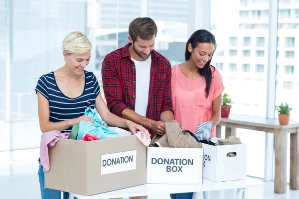 Smiling young friends volunteers separating clothes — Stock Photo, Image