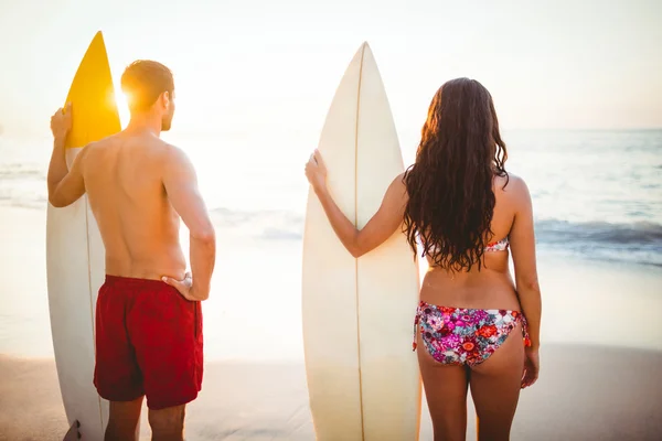 Pareja sosteniendo tablas de surf mirando al océano — Foto de Stock