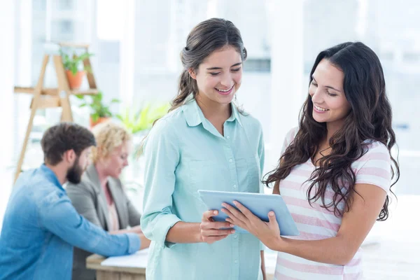 Mujeres de negocios sonrientes usando una tableta con colegas —  Fotos de Stock