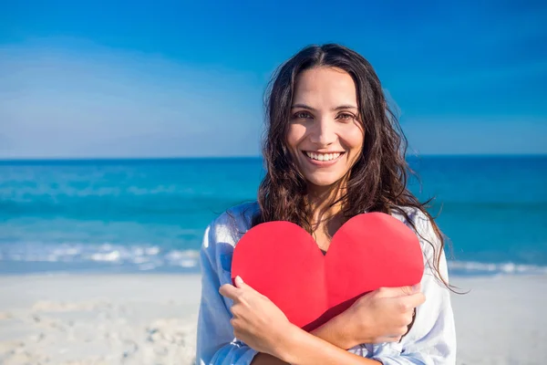 Smiling woman holding heart card at the beach — ストック写真