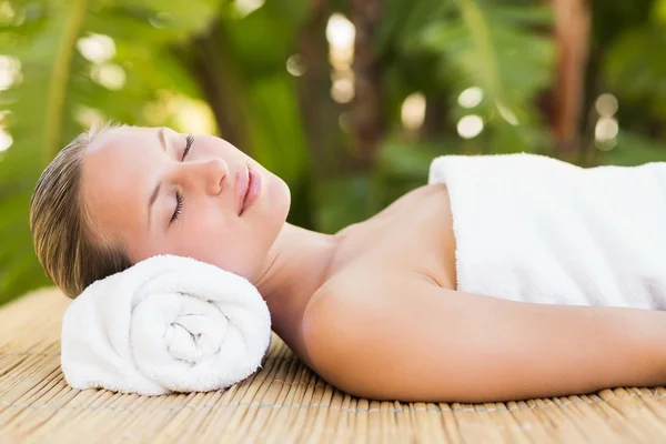 Blonde on bamboo mat with flowers at spa — Stok fotoğraf