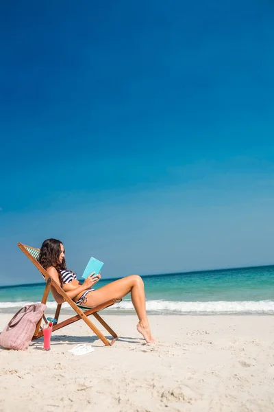 Bonita morena leyendo un libro sobre tumbona — Foto de Stock